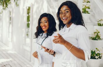 Stylish black doctors in a white uniform. Ladies with stethoscope. Two girls use the tablet and book